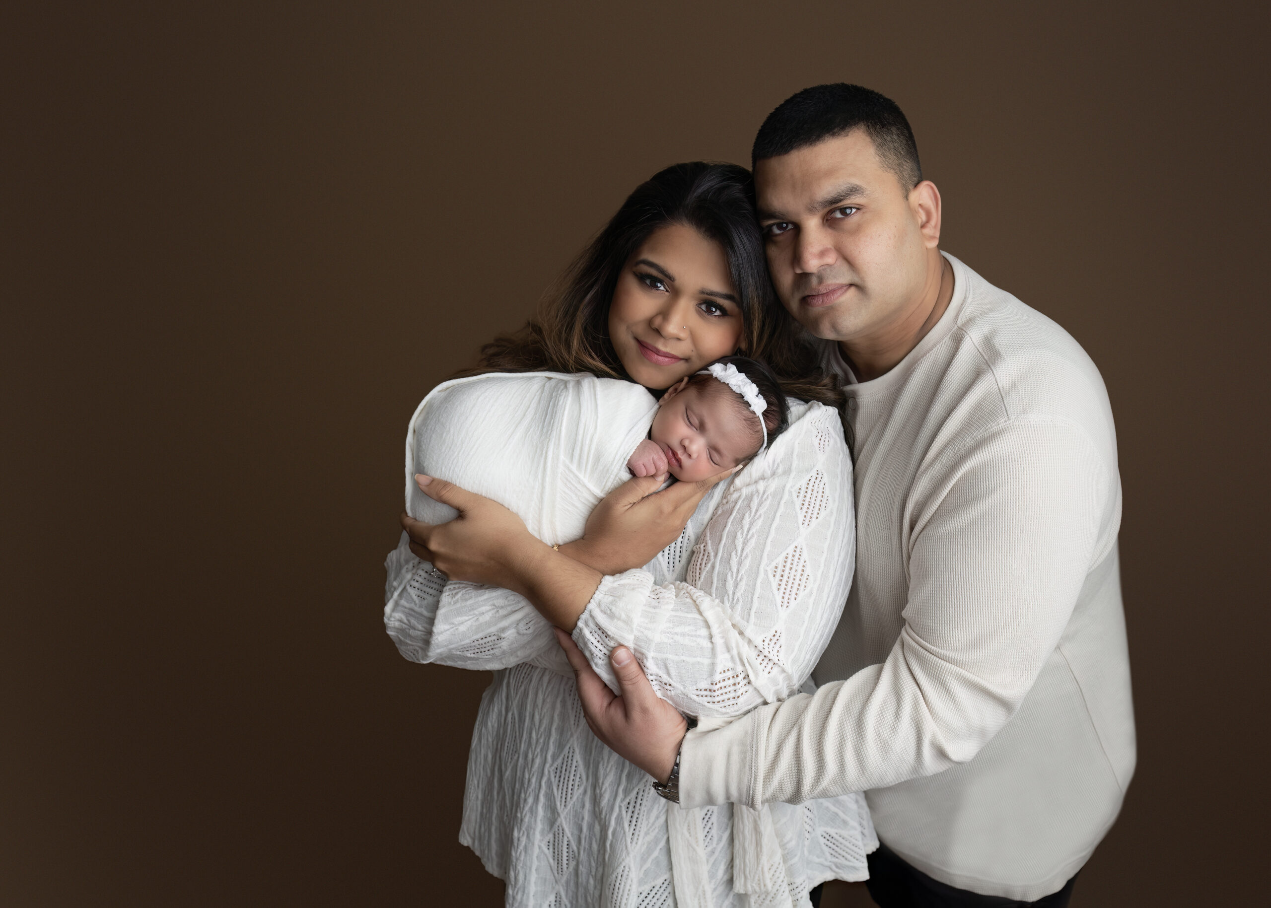 A heartwarming moment of a family cuddling with their newborn baby, styled in soft neutral tones, captured in a luxury photography session in Brantford, Ontario