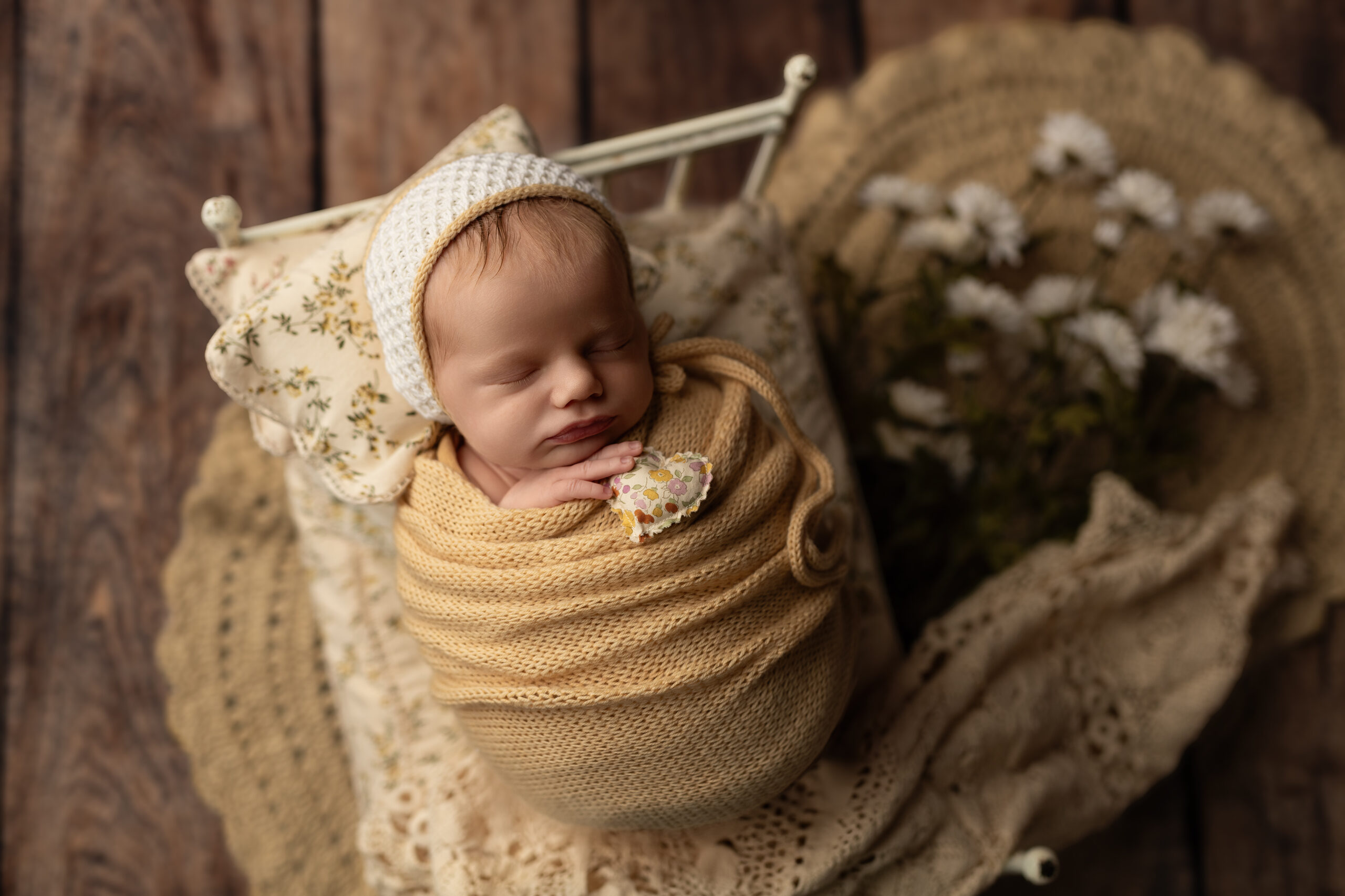 Newborn baby wrapped in a cozy neutral-colored swaddle, peacefully sleeping on a soft, textured blanket at Meraki Photographic Creations studio in Paris, Ontario.