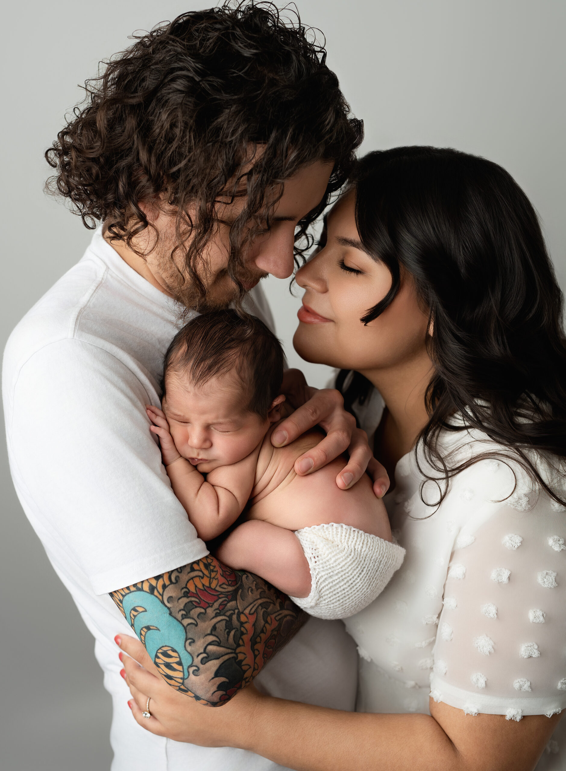 Newborn baby peacefully sleeping in the loving arms of parents, showcasing a tender family moment. Discover the beauty of timeless family photography. This portrait features a newborn baby sleeping peacefully in the loving arms of parents, captured by Meraki Photographic Creations in Paris, Ontario.